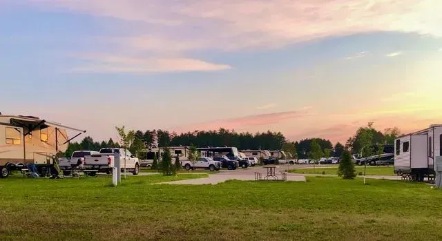 RV campground at dusk with trailers, grass, and trees under a pink and blue sky.