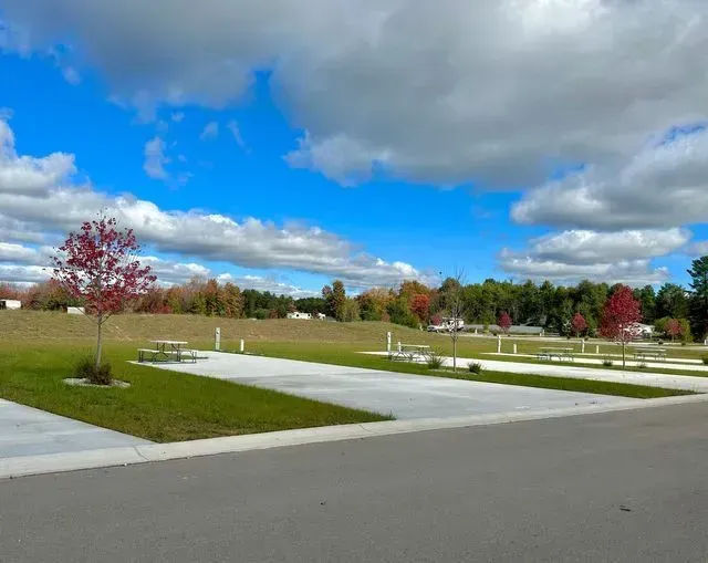 Empty RV campsites with concrete pads, green grass, and trees with fall foliage under a blue sky.