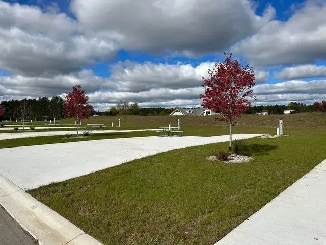 Empty RV campsites with red trees, green grass, and cloudy blue sky.