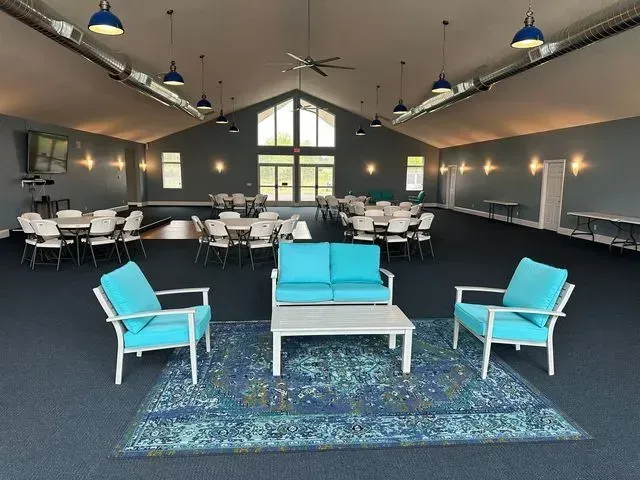 Large, open event space with blue furniture and tables; neutral walls, high ceiling, and natural light.