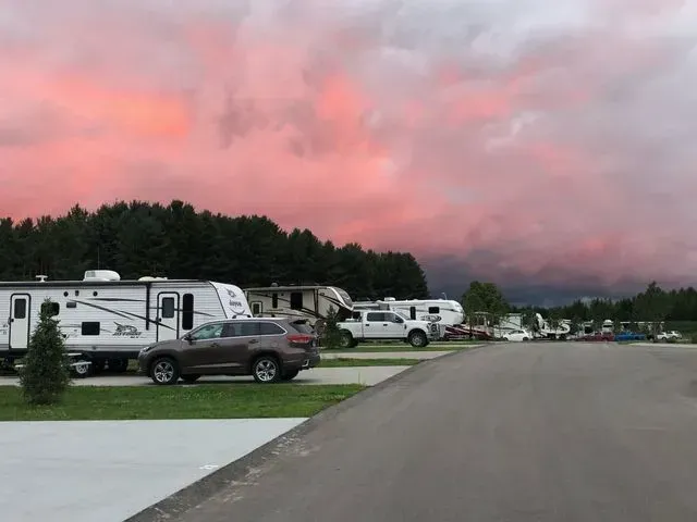 RV park with trailers, cars, and a pink and purple sunset sky.