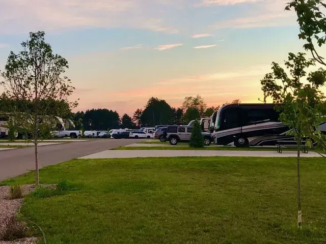 RV park at sunset, with RVs, cars, and trees under a colorful sky.