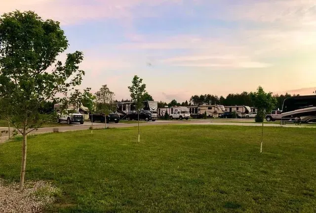 Lawn with RVs and cars at a campground under a cloudy sky at sunset.
