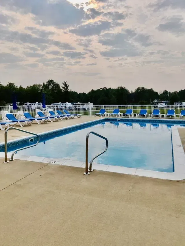 Swimming pool with blue water, white concrete deck, and blue and white lounge chairs. Overcast sky.