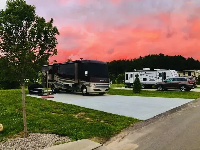 RV park at sunset, featuring a large motorhome and campers against a vibrant red and pink sky.