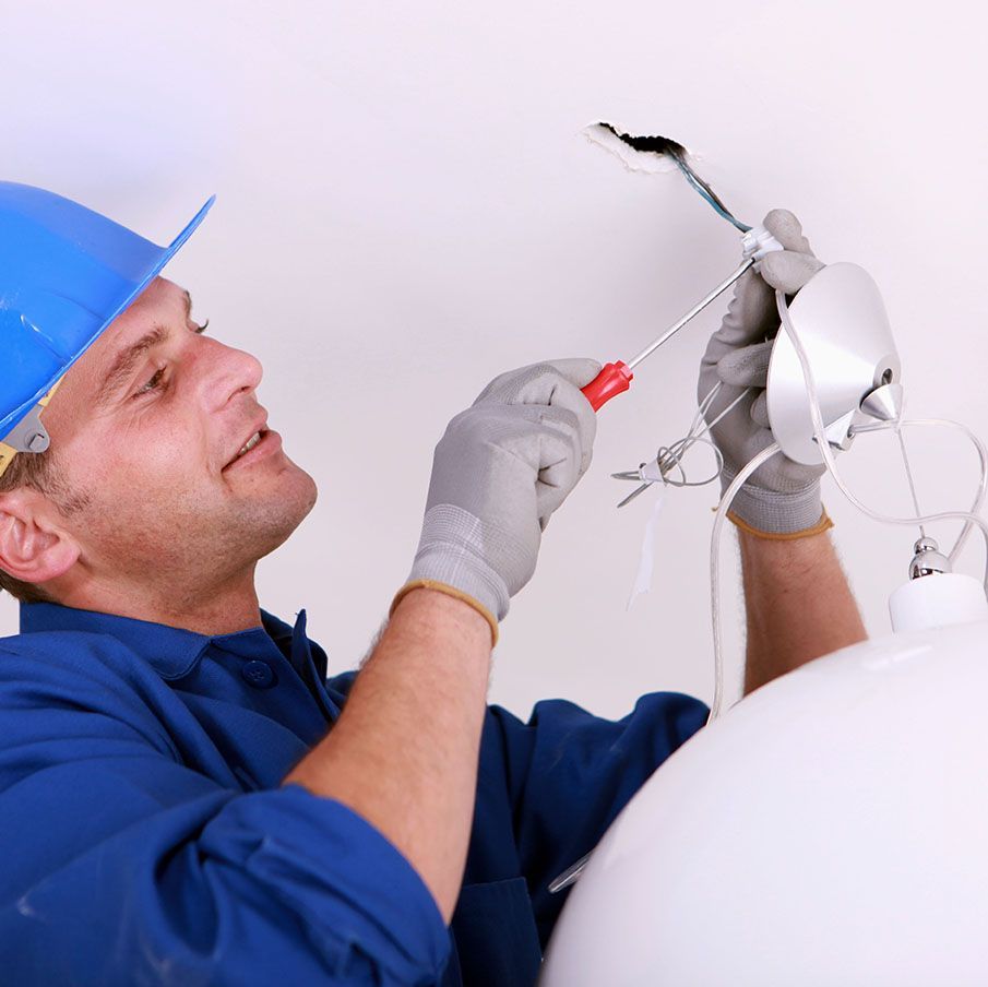 A man wearing a hard hat and gloves is working on a light fixture