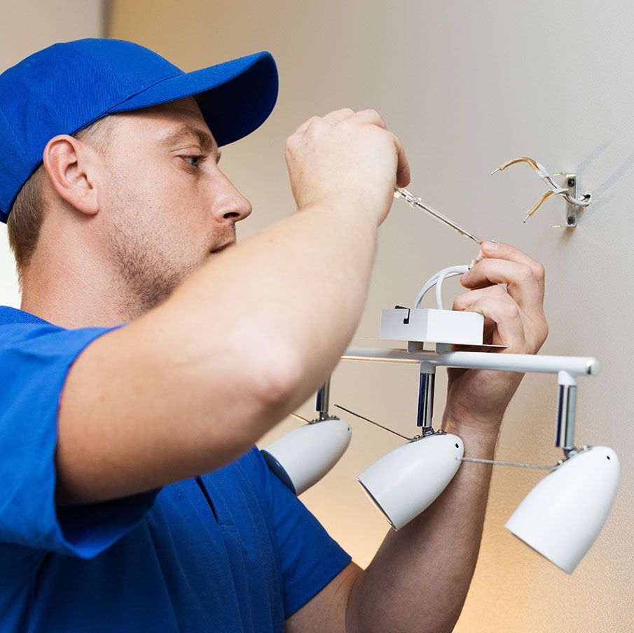 A man in a blue hat is installing a light on a wall