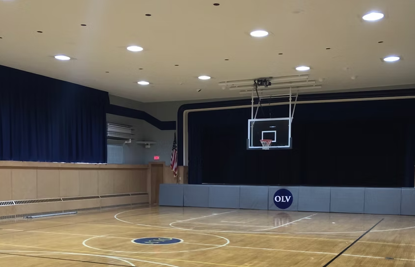An empty gym with a basketball hoop and a sign that says oly