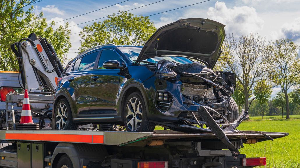 Damaged blue SUV loaded on a tow truck with front-end crash damage and open hood