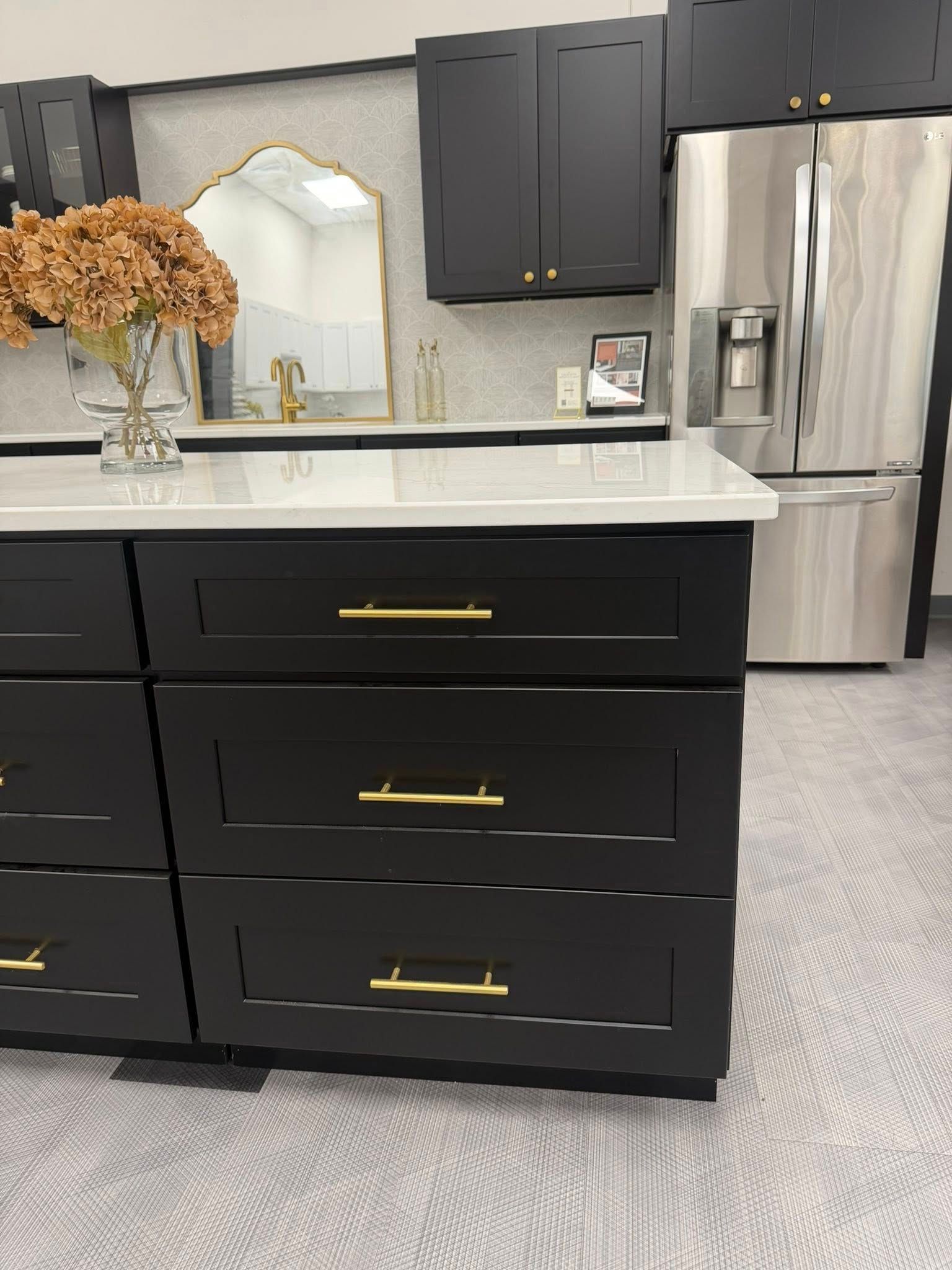 Black kitchen cabinets with gold hardware, white countertop, stainless steel refrigerator.