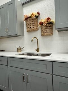 Gray kitchen cabinets, white countertop, gold faucet, and baskets of flowers.