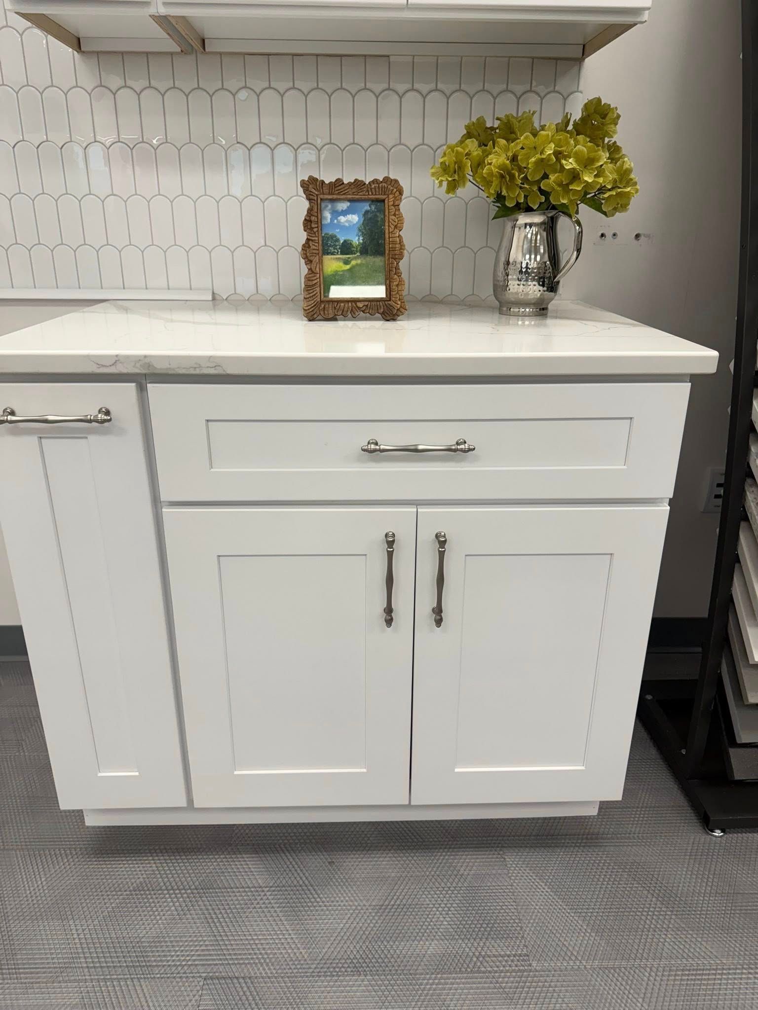 White cabinet with countertop, artwork, flowers. White tile background, silver hardware.