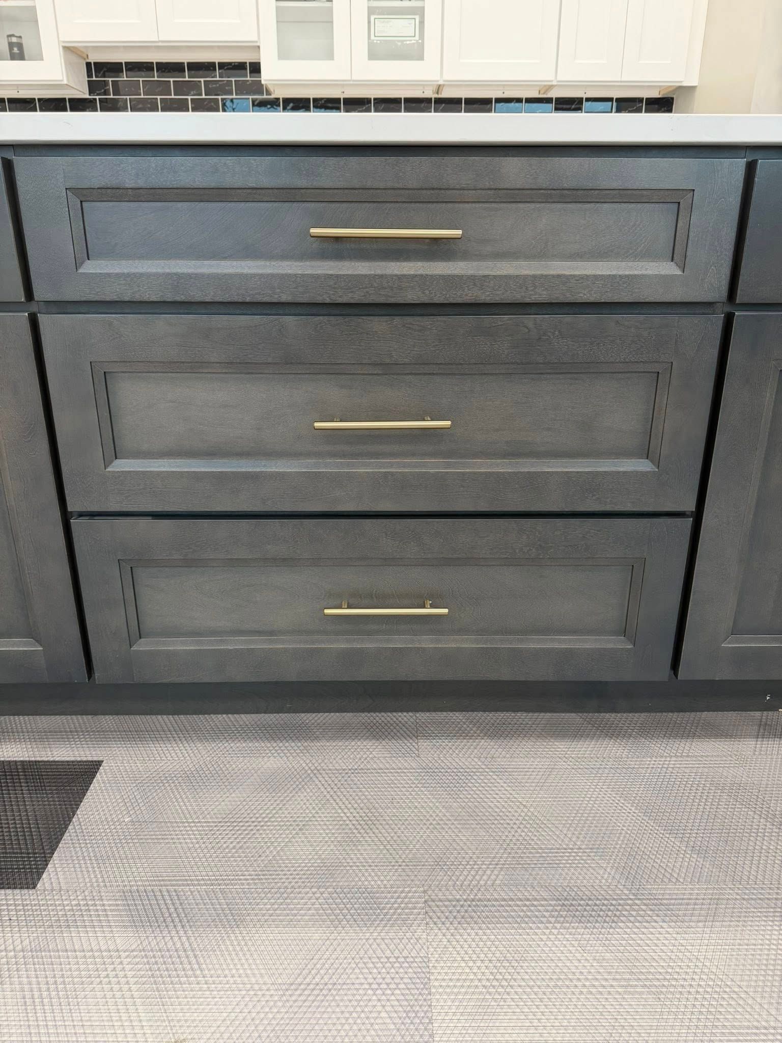 Gray kitchen drawers with gold handles against a light patterned floor.