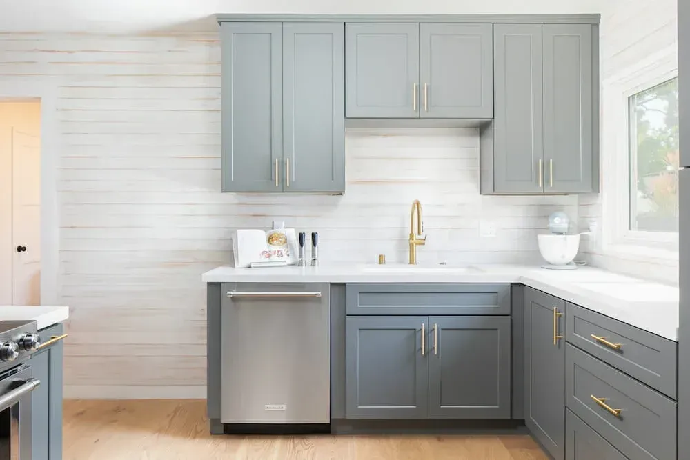 Gray kitchen cabinets with gold hardware and stainless steel appliances against a white backdrop.