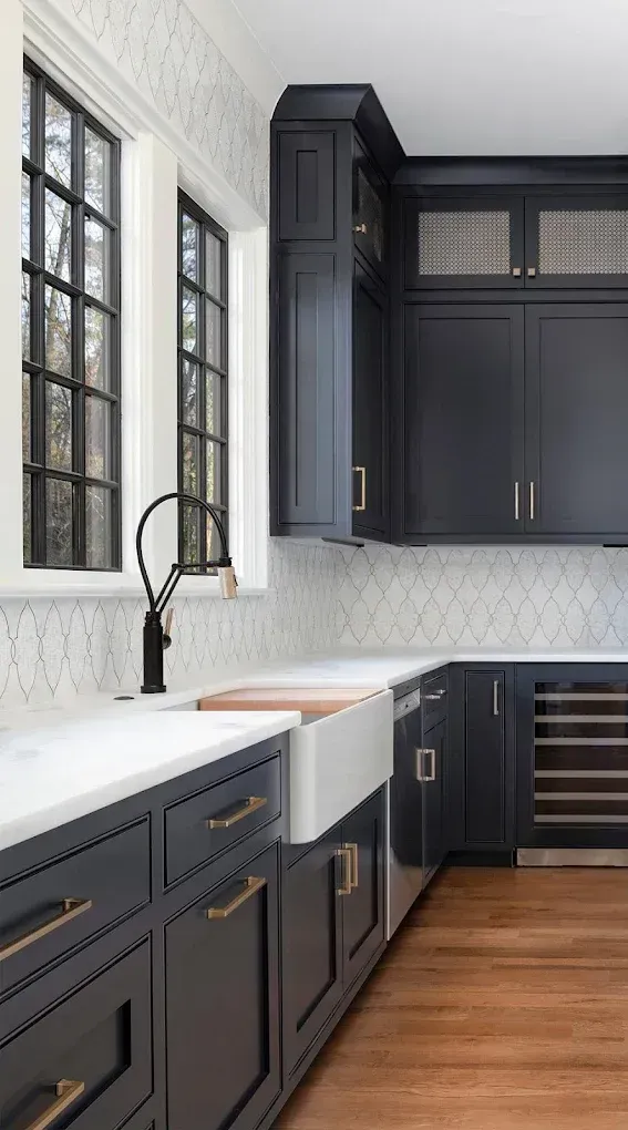 Dark blue kitchen cabinets with white countertops, sink, and backsplash near a window.