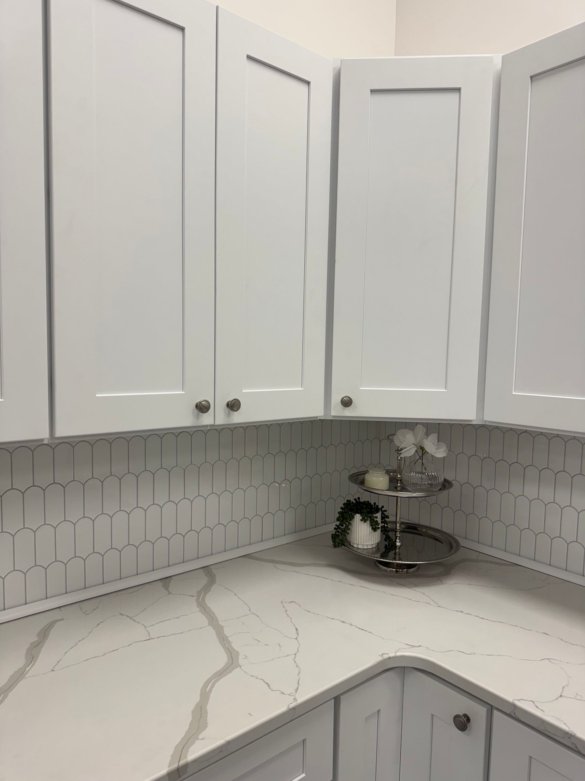 White kitchen cabinets in a corner with white and gray backsplash and countertop.