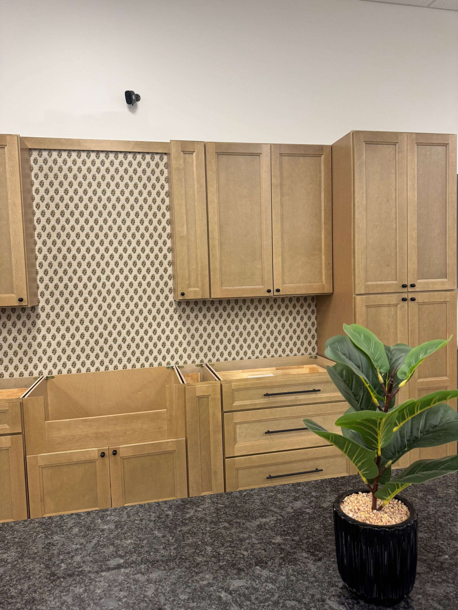 Kitchen cabinets in a display with a mosaic backsplash, a plant, and a dark countertop.