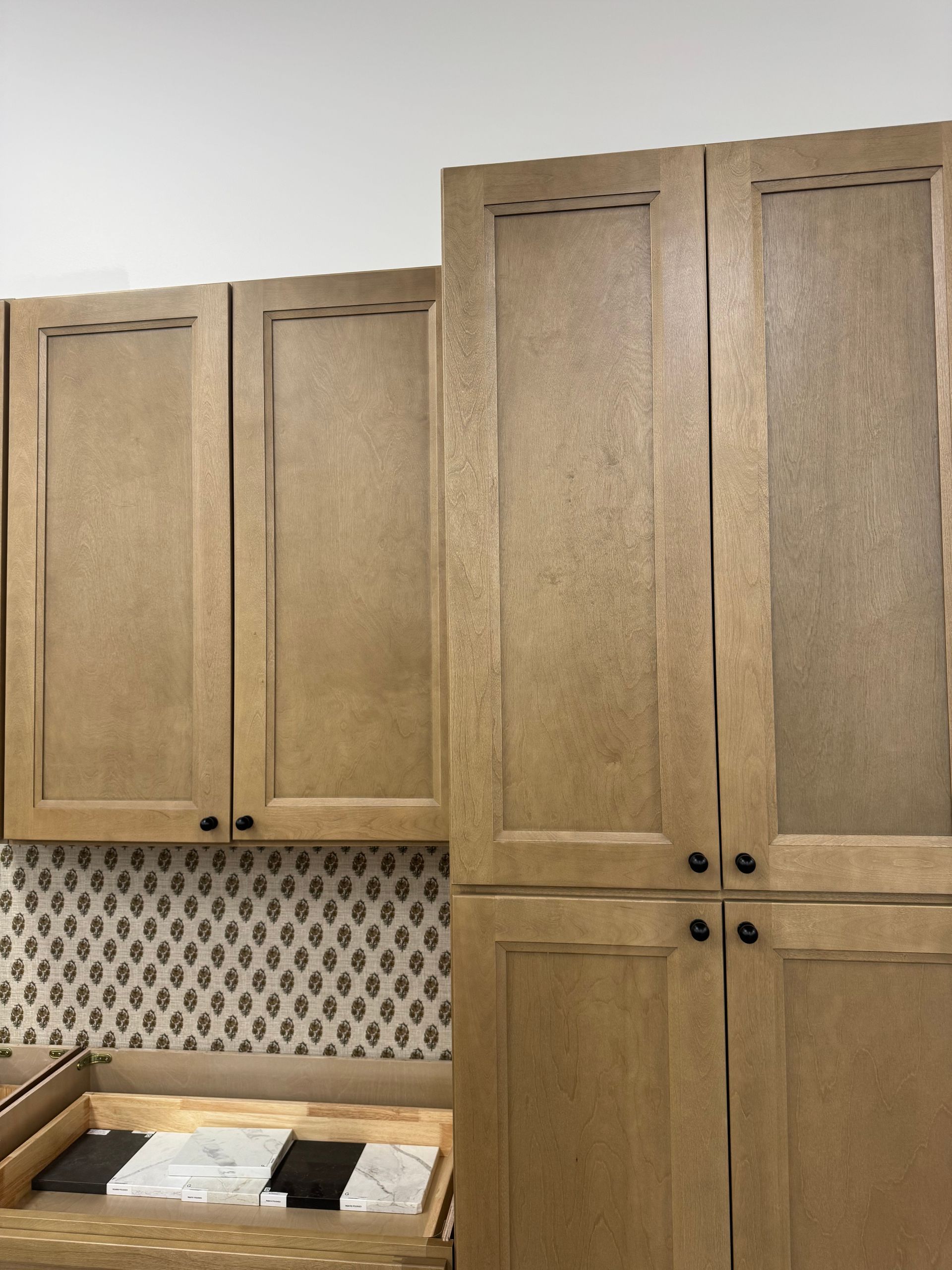 Light brown kitchen cabinets with black knobs, above patterned backsplash.