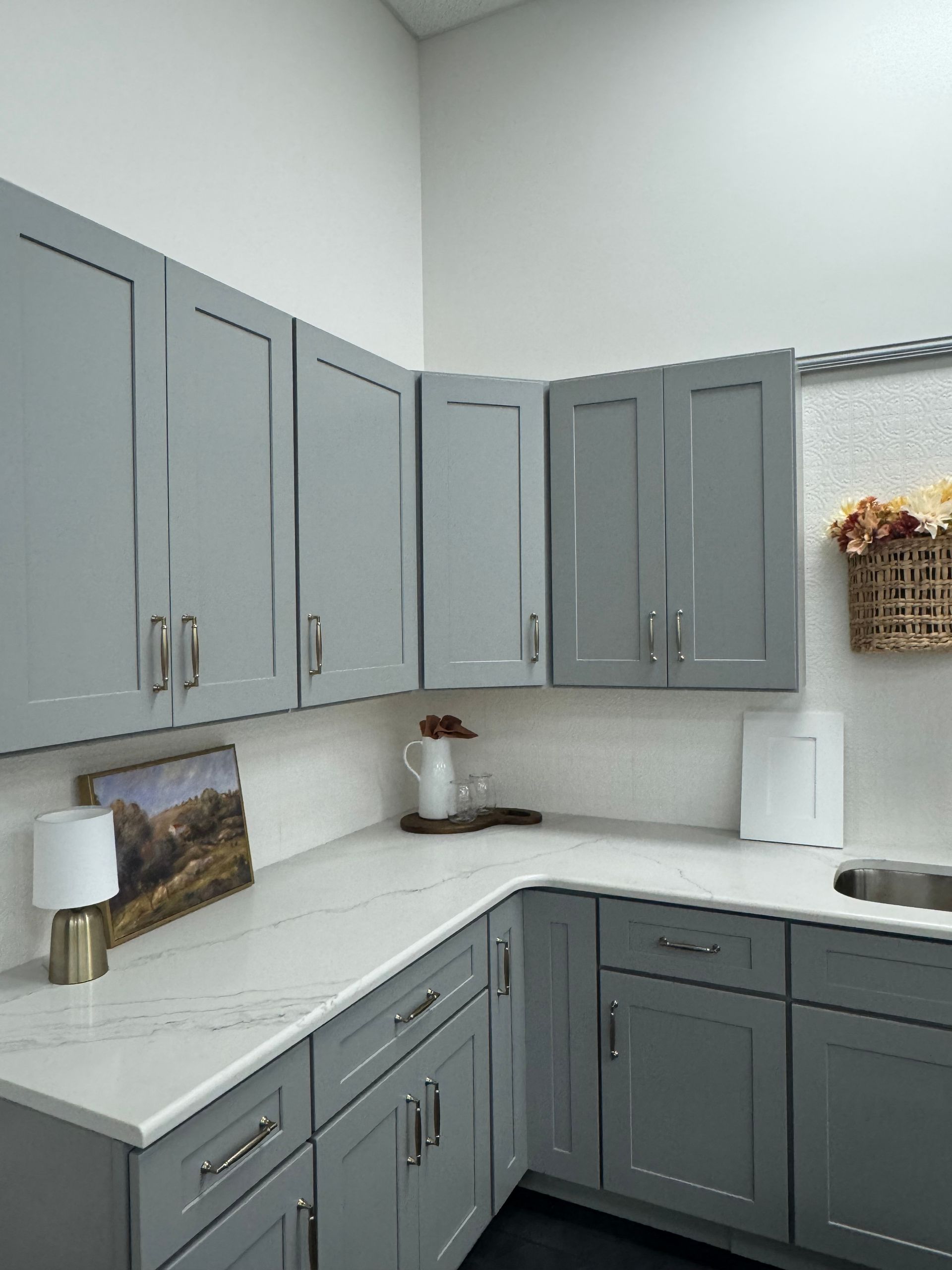 Gray kitchen cabinets with white countertop and sink.