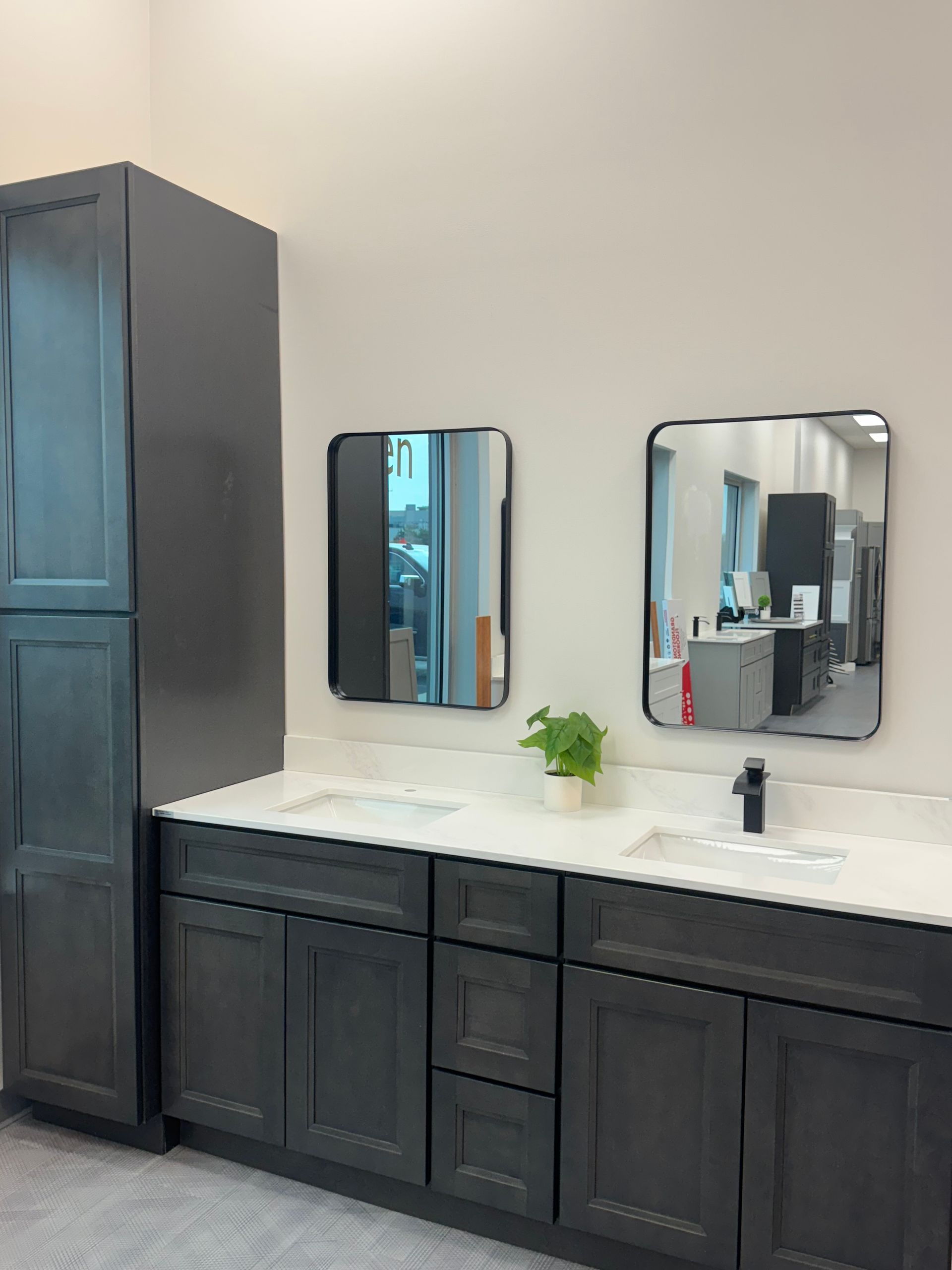 Dark gray bathroom vanity with two mirrors, a tall cabinet, and a potted plant.