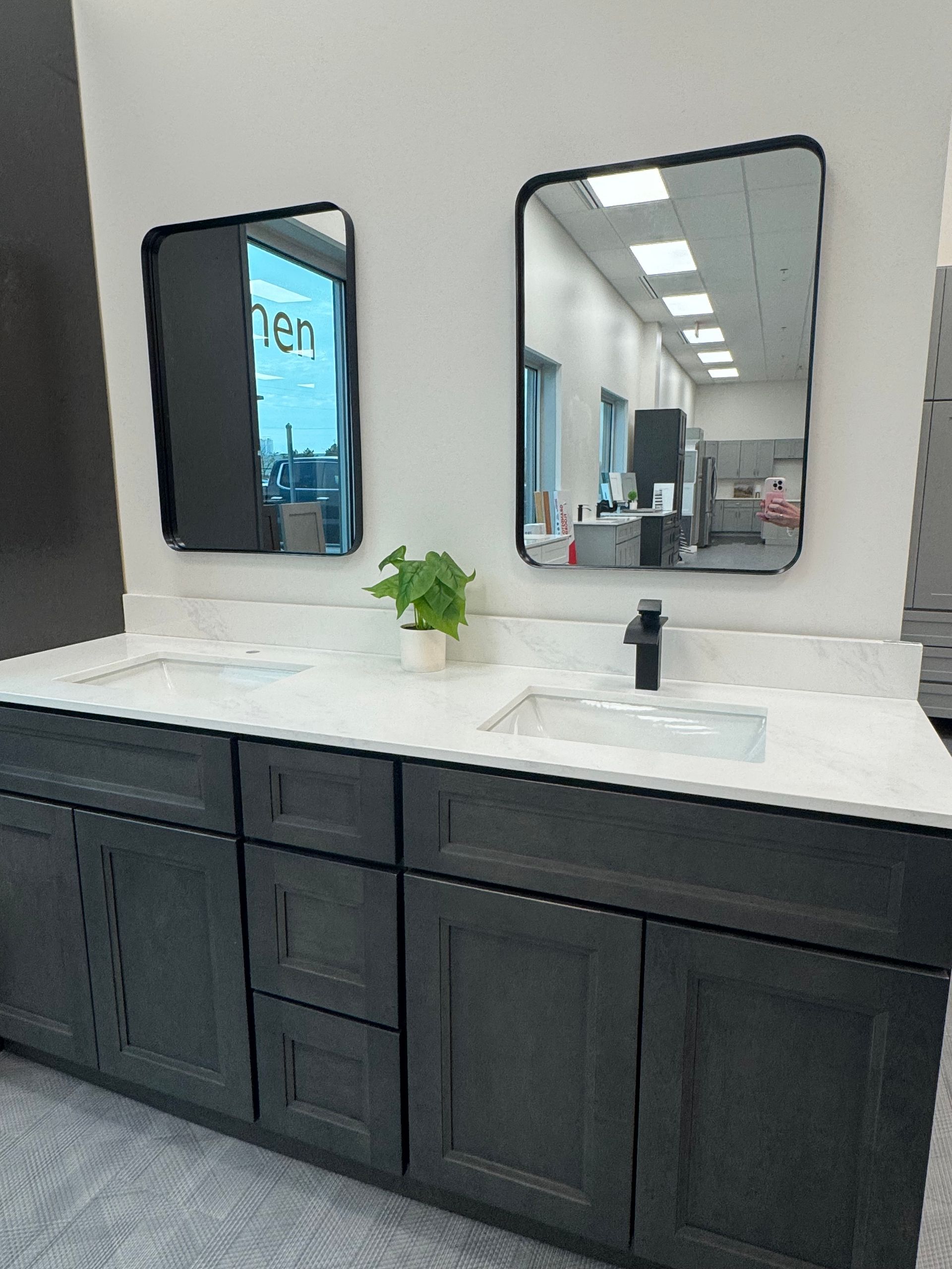 Bathroom vanity with two black-framed mirrors, a black faucet, and gray cabinets.