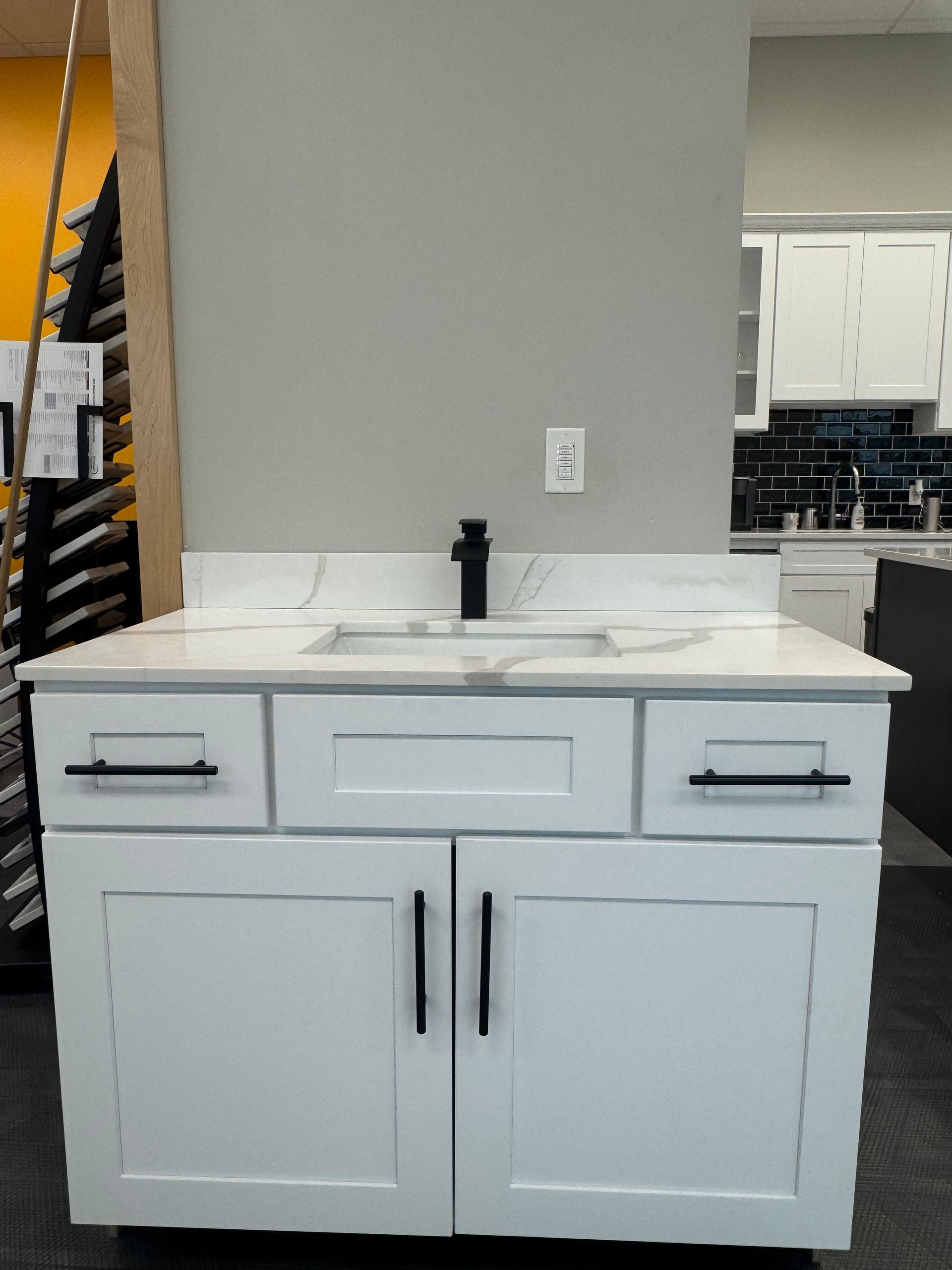 White bathroom vanity with black hardware, white countertop, and black faucet.