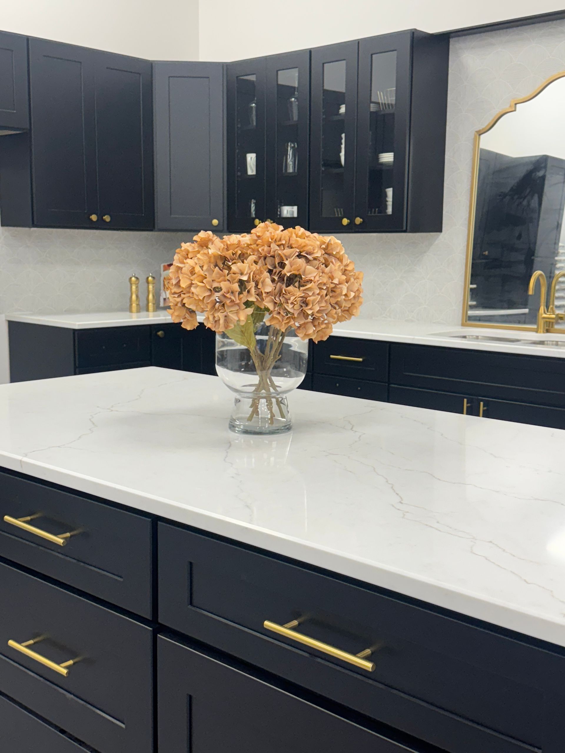 Black kitchen cabinets with gold hardware, white countertops, and floral arrangement.