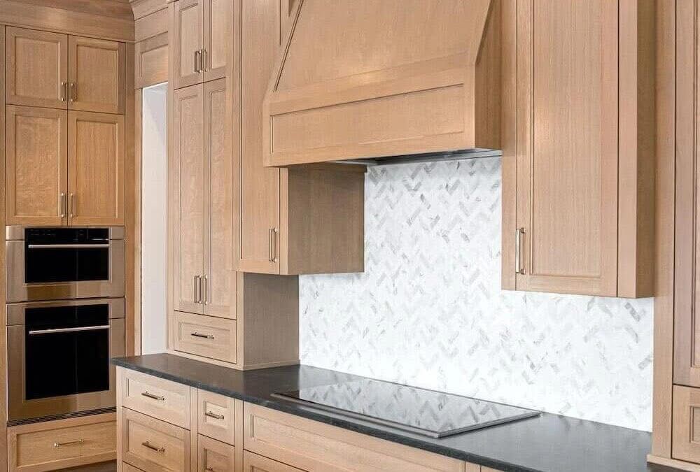 Kitchen with light wood cabinets, black countertop, and herringbone tile backsplash.