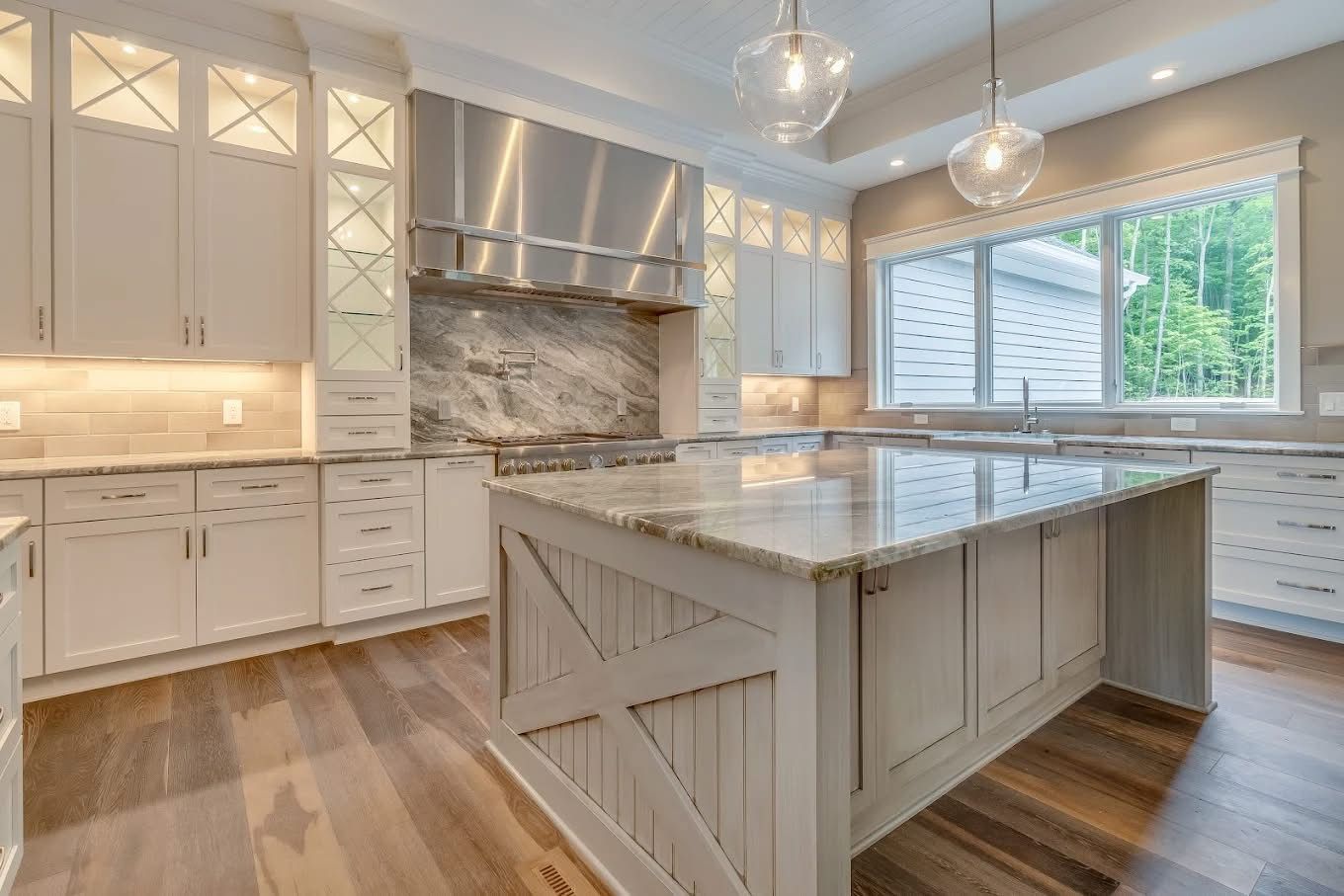 Elegant white kitchen with large island, granite countertops, stainless steel hood, and hardwood floors.