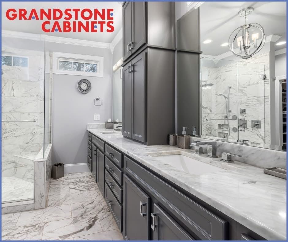 Modern bathroom with gray cabinets, marble countertops, and a glass shower.