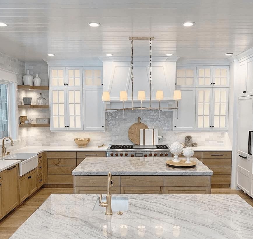 Modern kitchen with white and wood cabinets, marble countertops, and a central island with pendant lighting.