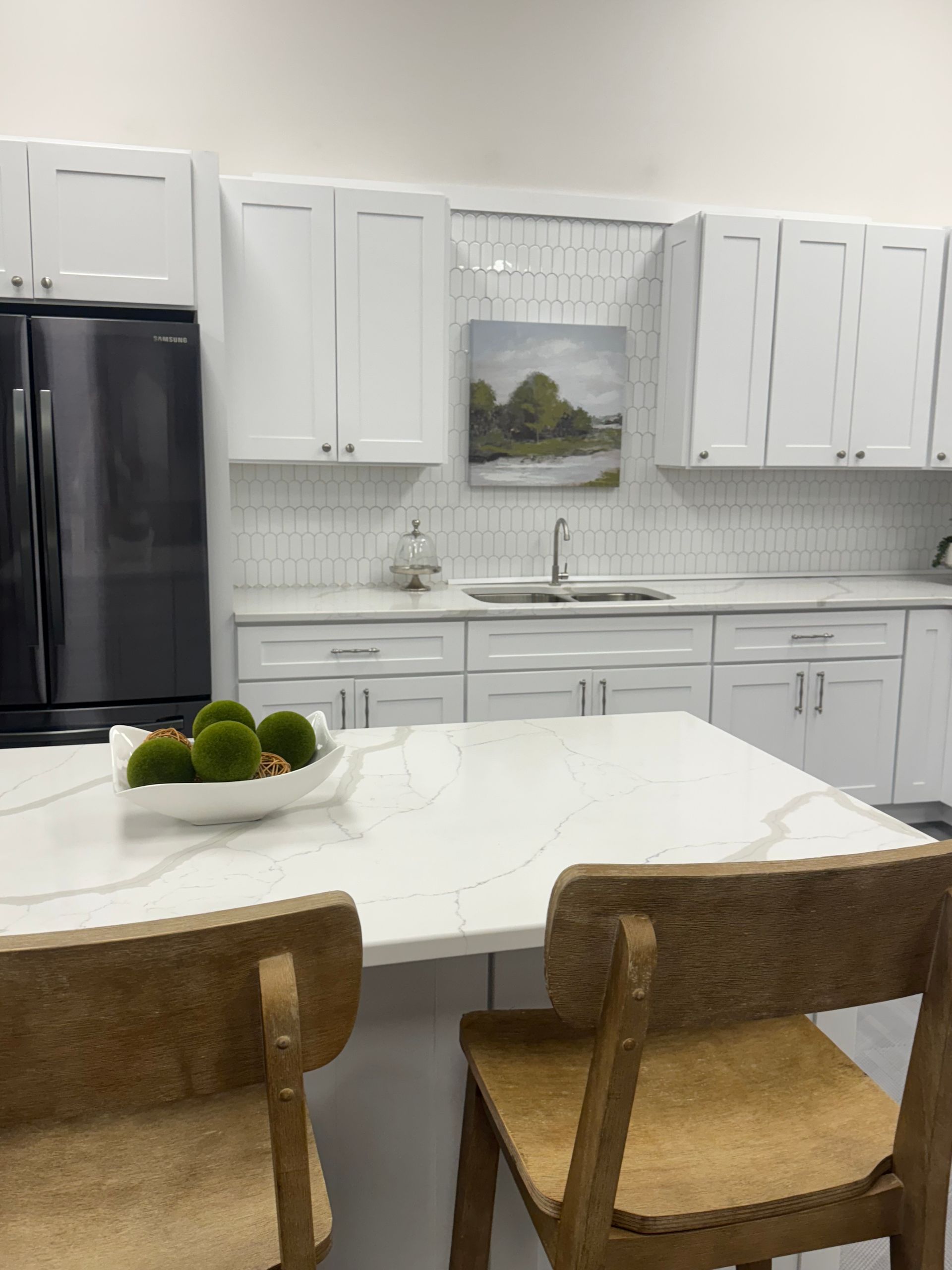 White kitchen with island, black refrigerator, and two wooden bar stools.