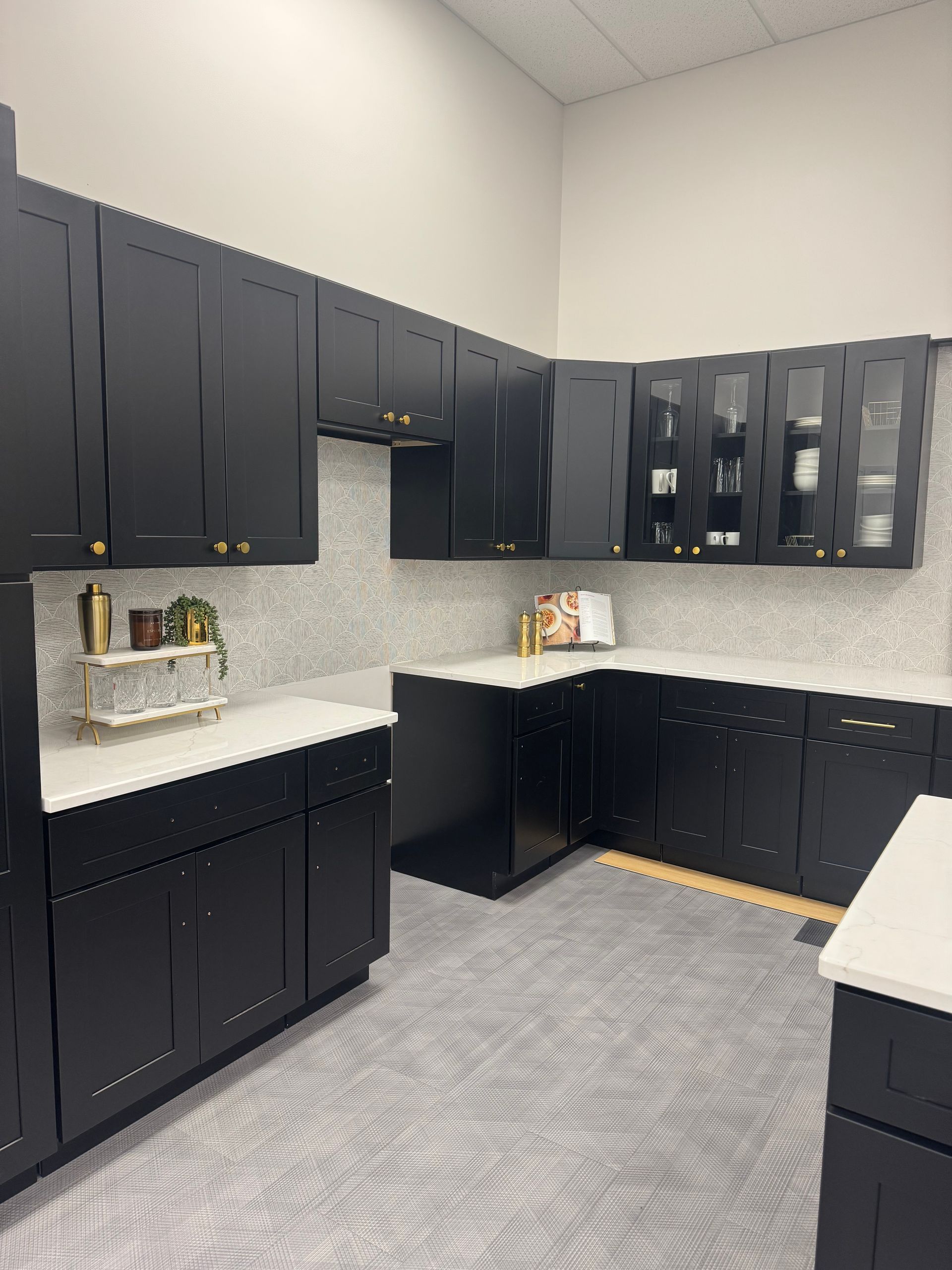 Black kitchen cabinets with white countertops, gray backsplash and flooring.