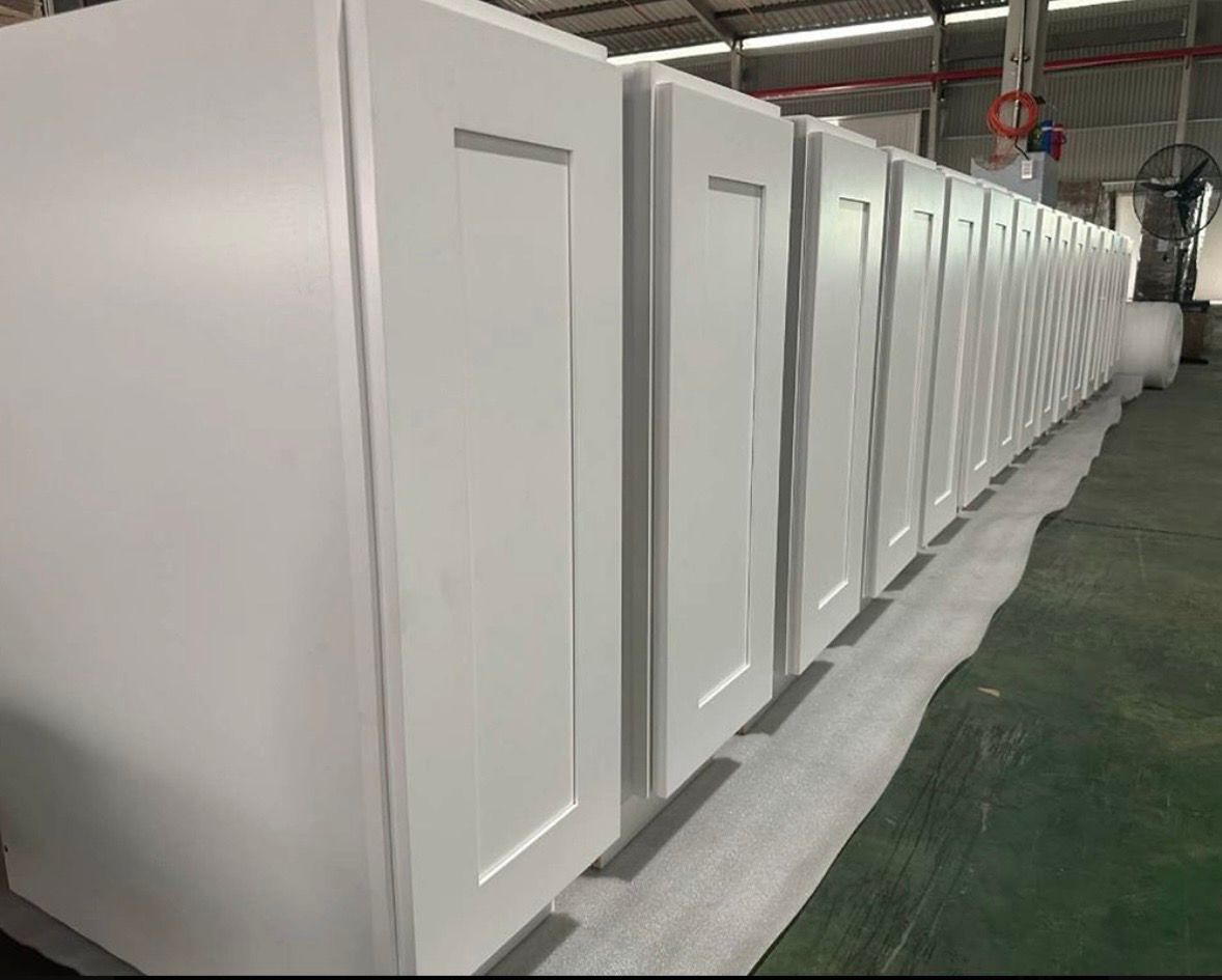 A row of white shaker-style cabinet doors arranged on the floor in a warehouse setting.