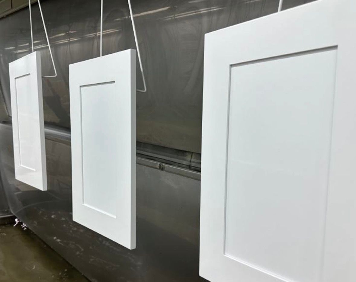 Three white cabinet doors hang vertically in a spray paint booth.