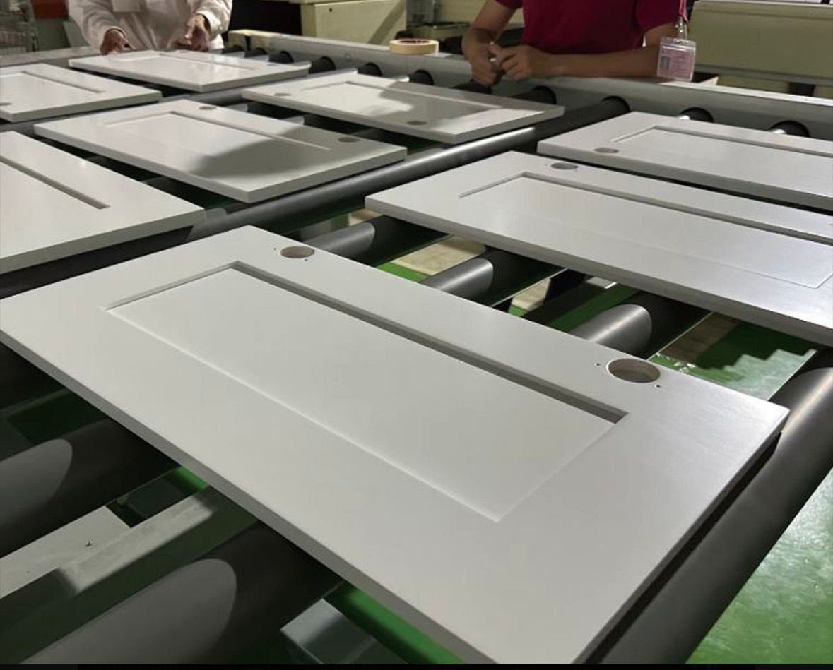 Workers process newly painted white cabinet doors along a factory conveyor line.