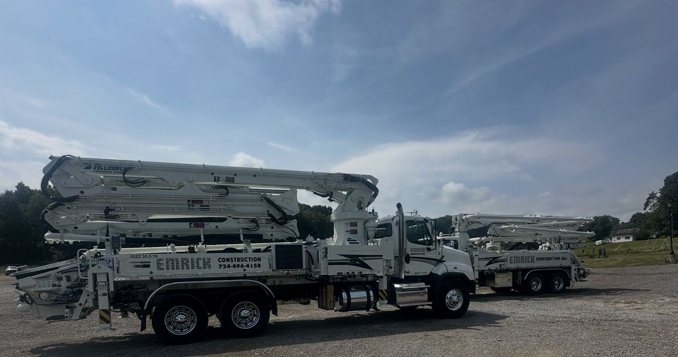 Two white concrete pump trucks parked outside on a sunny day.