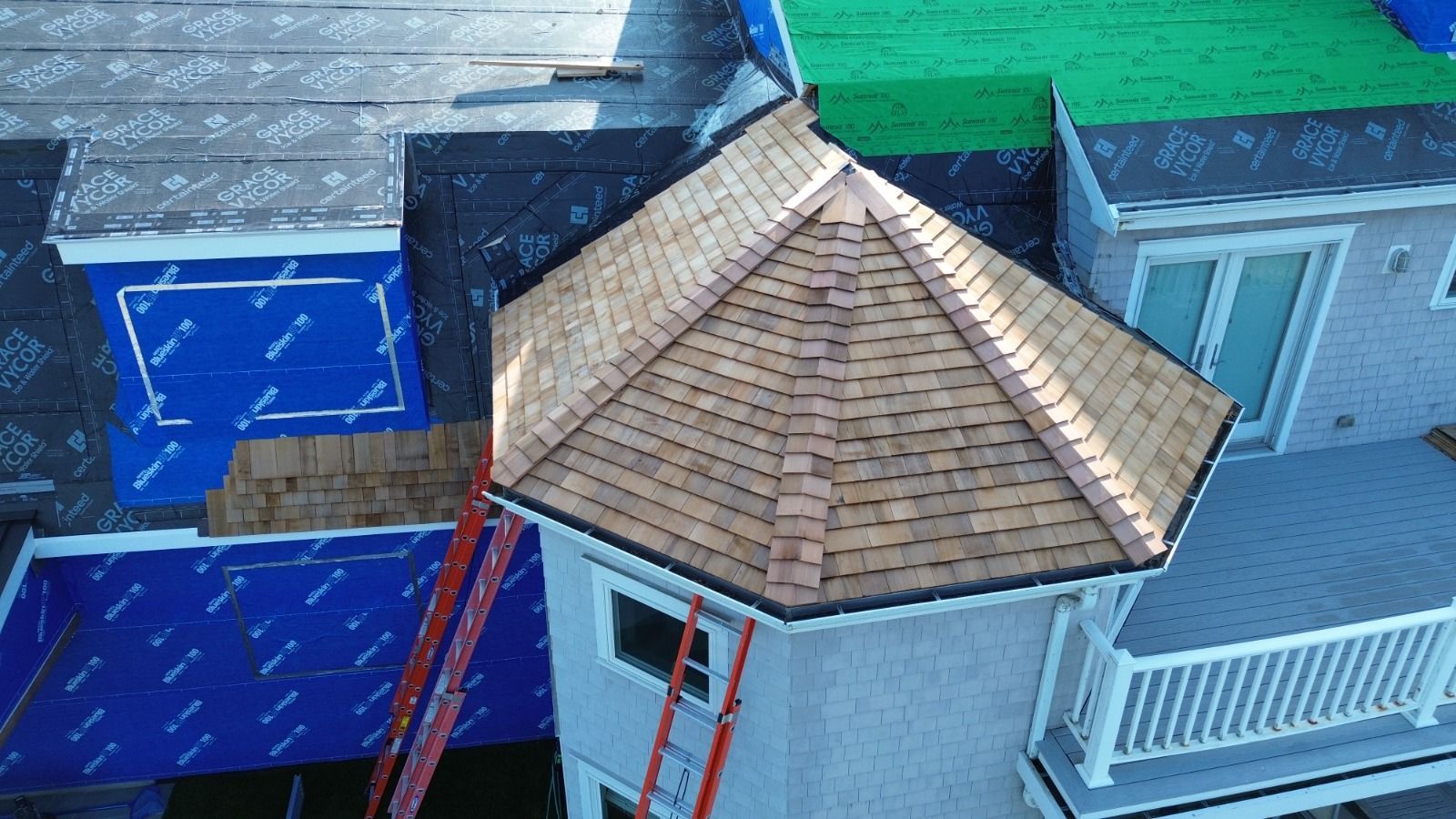 Roofing work in progress on a multi-story home, with a partially shingled turret and ladders visible.