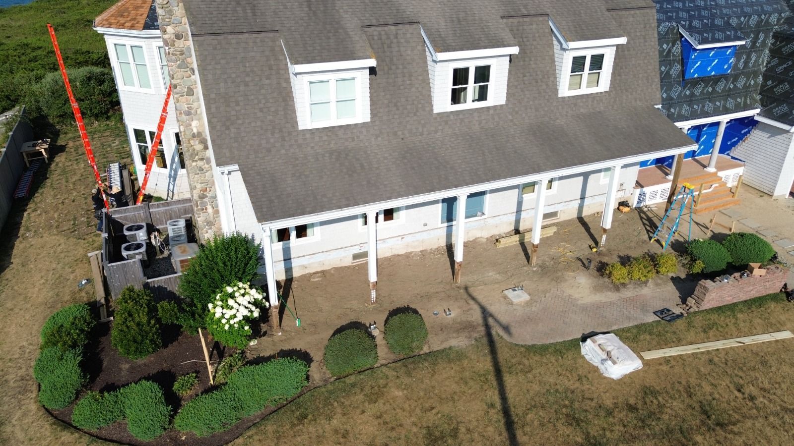 A white house with a gray roof and dormer windows. A red lift is set up near the side.