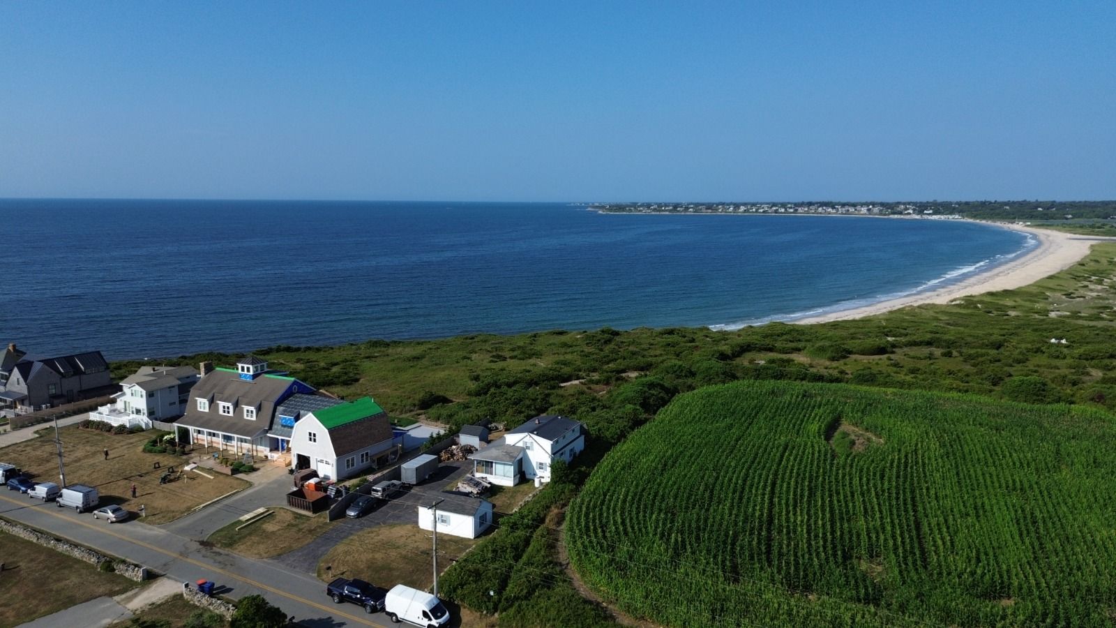 Aerial view of a beach with blue water, a sandy shore, and buildings along the coast on a sunny day.