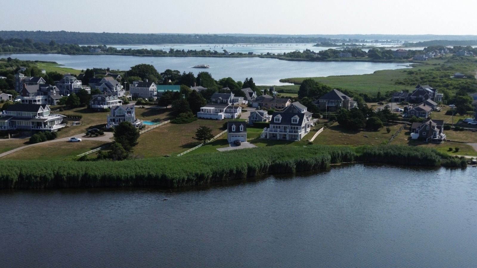 Houses line a waterfront. Calm water in foreground, bright sky.