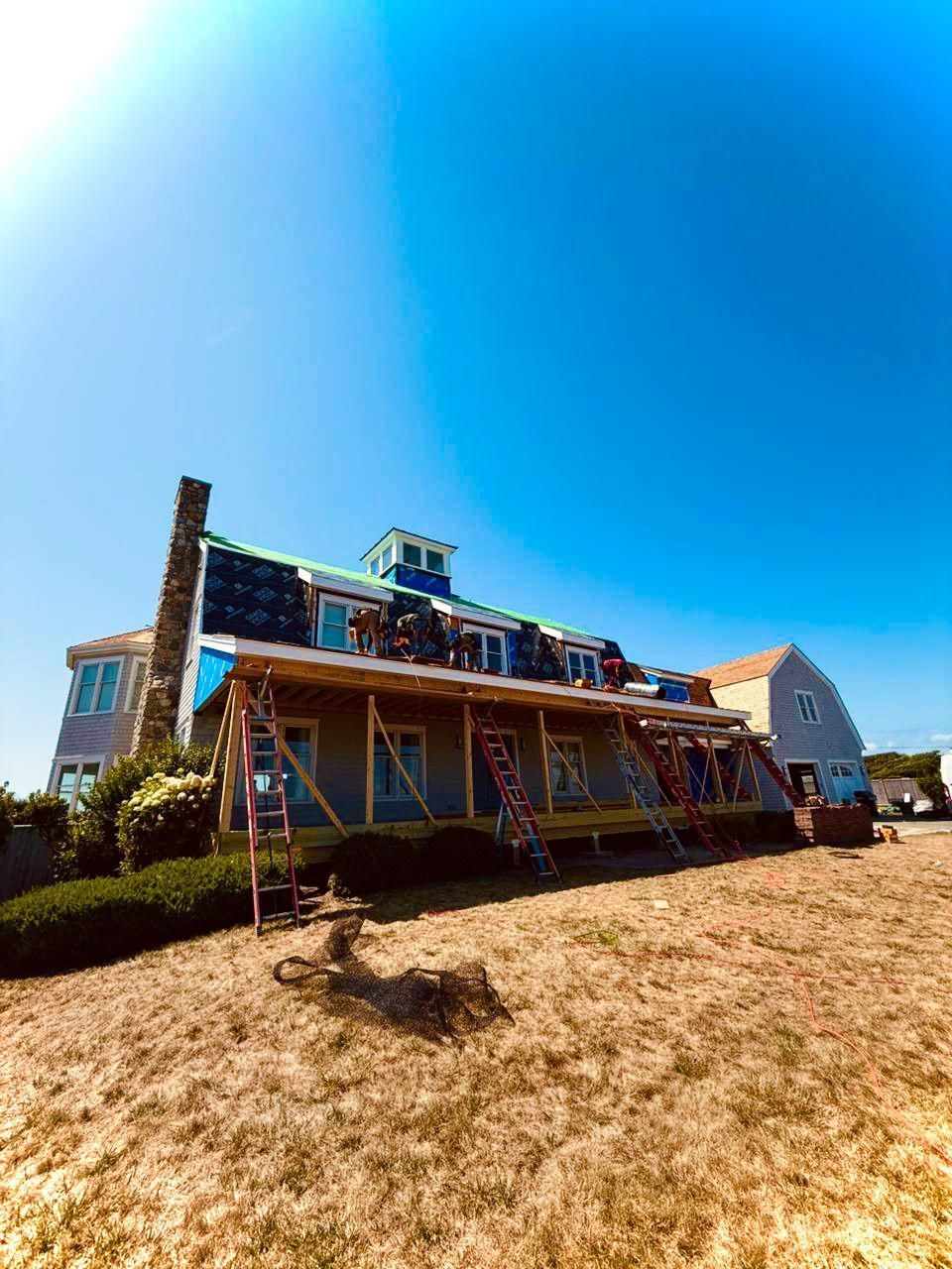 Roofers working on a blue-roofed house under a bright blue sky.