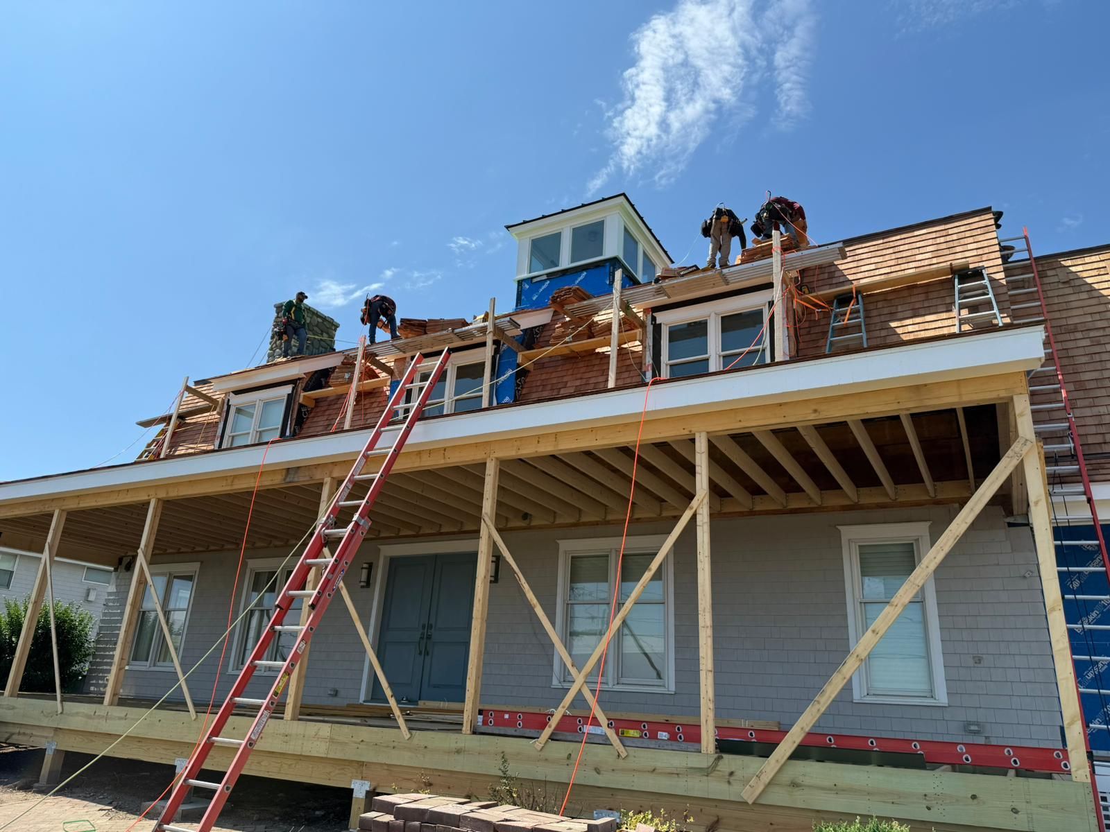 House under construction with workers on the roof, blue sky, wood frames, and ladders.
