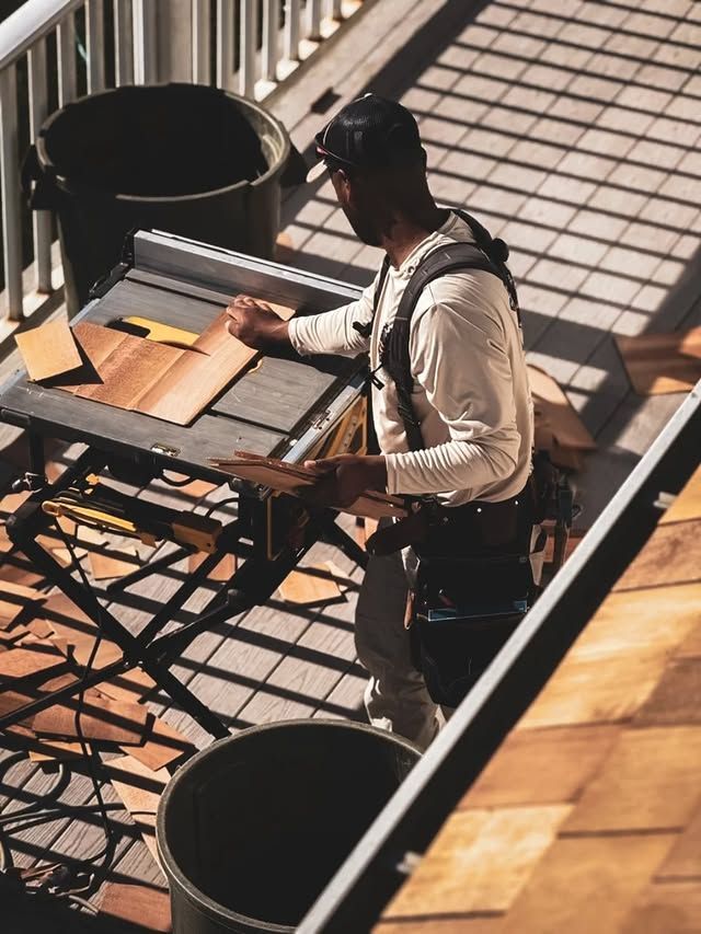 Man working on a rooftop, using a table saw to cut wood. He is wearing safety gear.