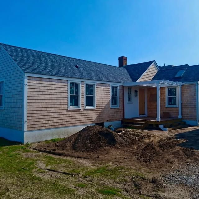 A light brown shingled house with a blue roof and a white pergola on a sunny day.