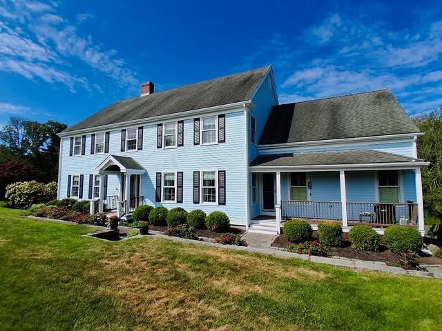 Blue two-story house with black shutters, porch, and green lawn under a blue sky.