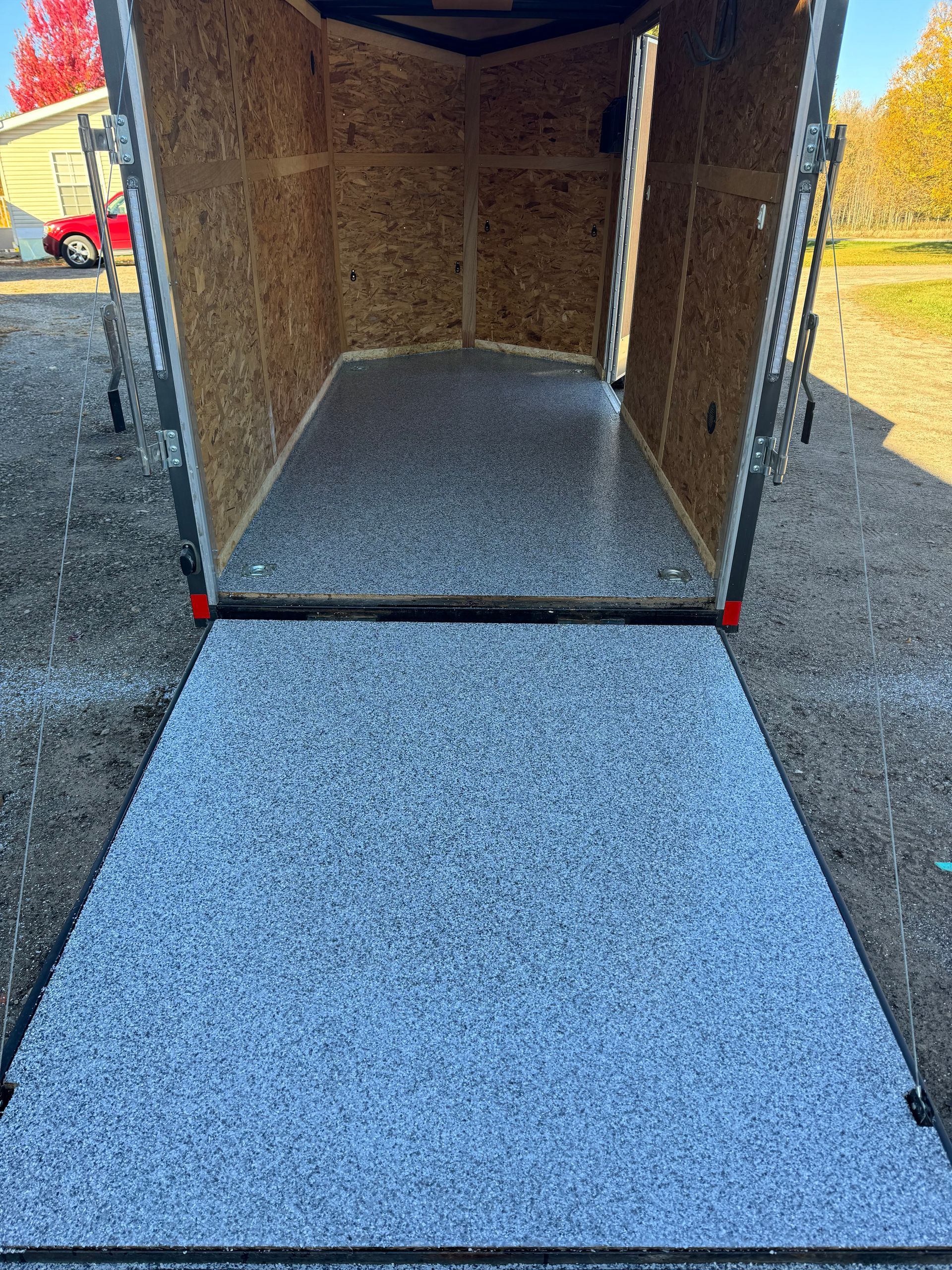 Wooden enclosed structure outdoors on gravel, with a concrete-coated floor inside.