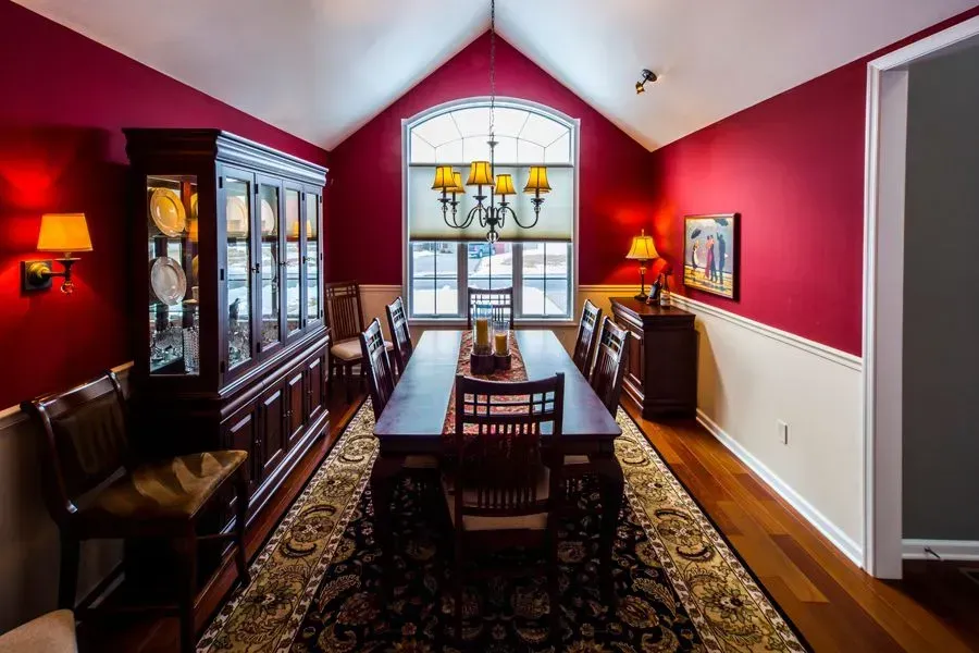 Formal dining room with red walls, wooden furniture, long table, and chandelier.