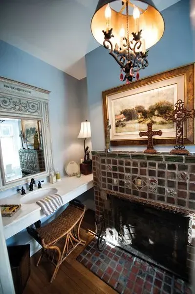 Bathroom with vanity, fireplace, and decorative chandelier; blue walls, ornate mirror, and artwork.