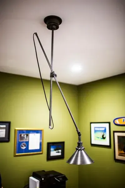 Silver adjustable desk lamp suspended from a ceiling in a green-walled office.